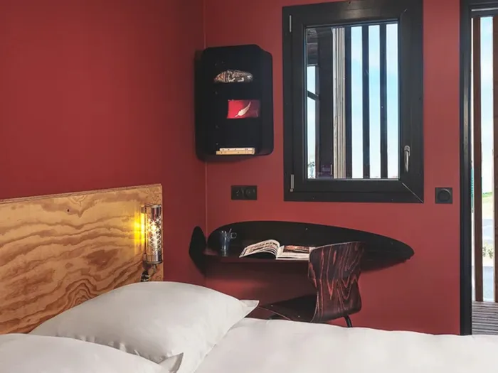 Room at the Eklo hotel near Disneyland Paris, with red walls, a light wood headboard, a small wall-mounted desk and a window.