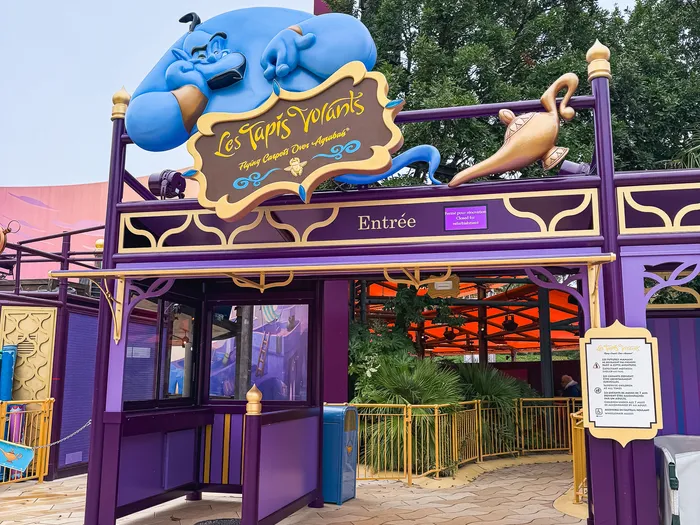 Génie bleu au-dessus de l’enseigne « Les Tapis Volants » à l’entrée de l’attraction, décor violet et or