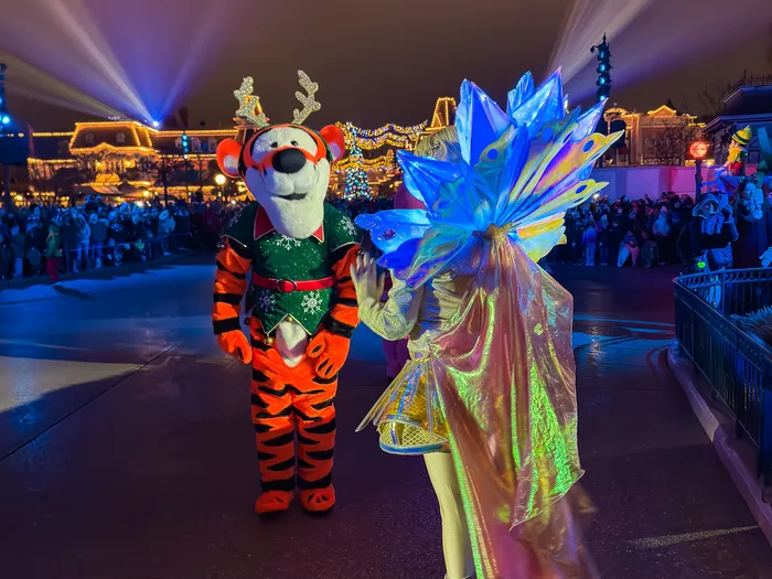 Tigrou déguisé en renne et danseuse en robe irisée pendant la parade de Noël, projecteurs sur Main Street.