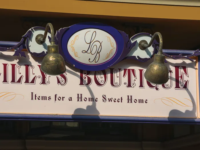 "Lilly’s Boutique" sign reading "Items for a Home Sweet Home", with an LB monogram and brass lamps, at Disneyland Paris.