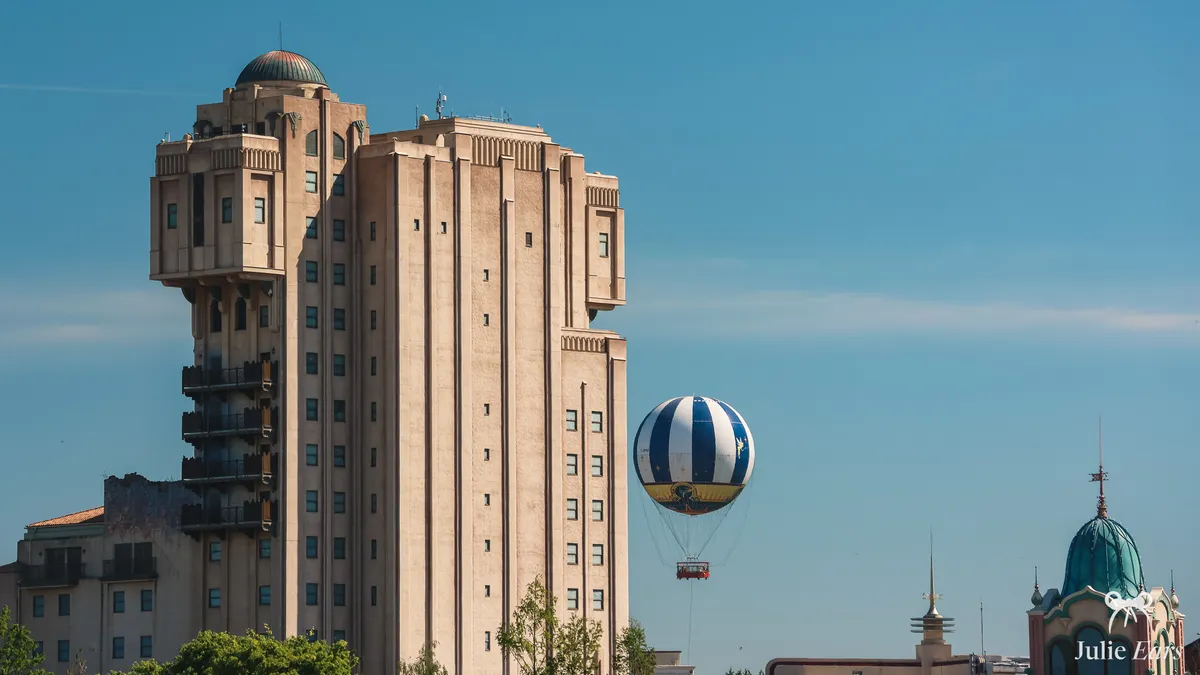 Hollywood Tower Hotel tower at Disneyland Paris under a blue sky, with its dome and Pueblo Deco lines and a striped tethered balloon in the distance