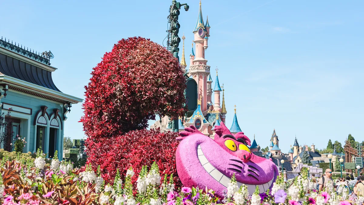 Cheshire Cat topiary with a grinning pink head and red foliage tail, with Sleeping Beauty Castle behind, at Disneyland Paris
