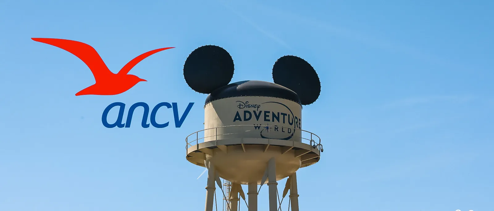 Château d’eau aux oreilles de Mickey du Parc Disney Adventure World sous un ciel bleu, avec le logo ANCV à la mouette rouge.