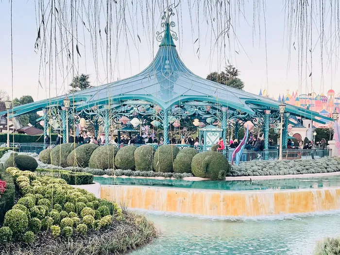 Vue d’ensemble du pavillon turquoise du Mad Hatter’s Tea Cups, entouré de haies taillées et d’un bassin à Fantasyland.