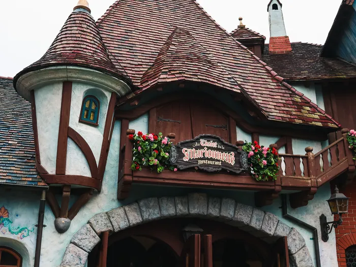 Façade à tourelle et colombages du restaurant Au Chalet de la Marionnette, à Fantasyland, avec balcon fleuri.