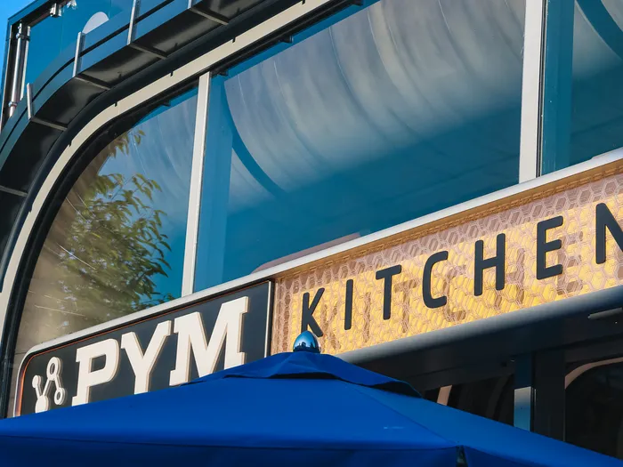 Enseigne lumineuse « PYM Kitchen » aux lettres alvéolées sur une façade métallique sombre, Avengers Campus.