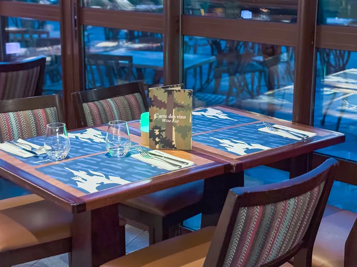 Table du Hunter’s Grill avec sets bleus et carte des vins, devant les baies vitrées donnant sur la terrasse