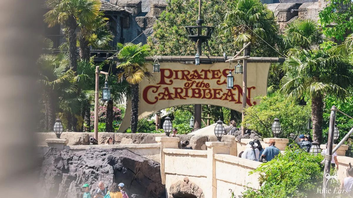 Pirates of the Caribbean sign painted on a sail between palm trees, above the stone bridge where visitors cross, at Disneyland Paris