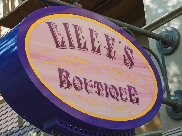 Oval "Lilly’s Boutique" sign with a purple border hanging on the shop facade, at Disneyland Paris.