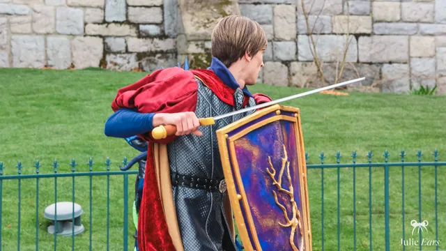 Le prince Phillip, en armure et cape rouge, épée et bouclier en main, près du château à Disneyland Paris.