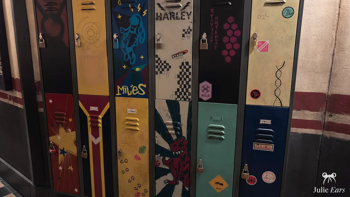 Colourful lockers named Miles and Harley in the Spider-Man W.E.B. Adventure queue, with W.E.B. and Stark stickers, an ant sign and a red dinosaur