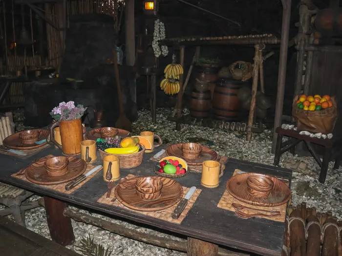 Table de bois dressée avec vaisselle sculptée, fruits et tonneaux dans le campement de La Cabane des Robinson