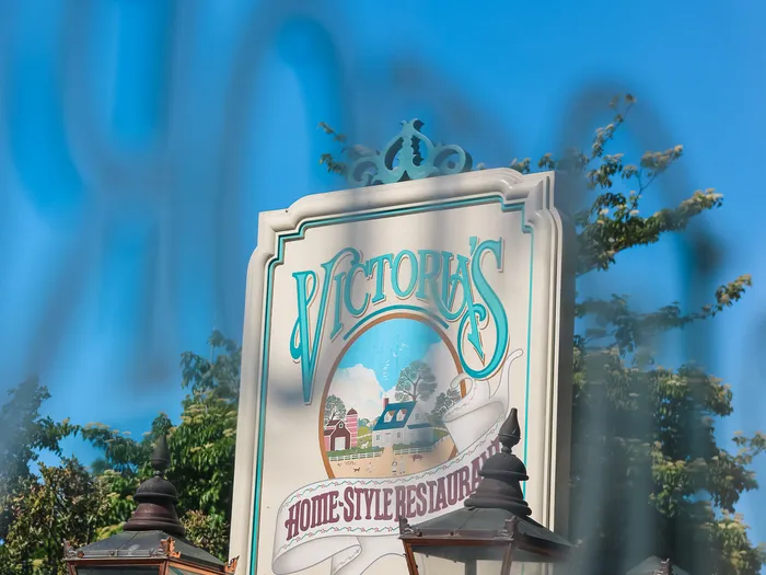 Enseigne suspendue de Victoria’s Home-Style Restaurant et lampadaires anciens sous un ciel bleu, Main Street USA.