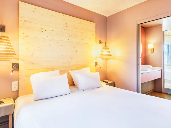 Chambre lumineuse avec tête de lit en bois clair et salle de bains attenante aux Villages Nature Paris.