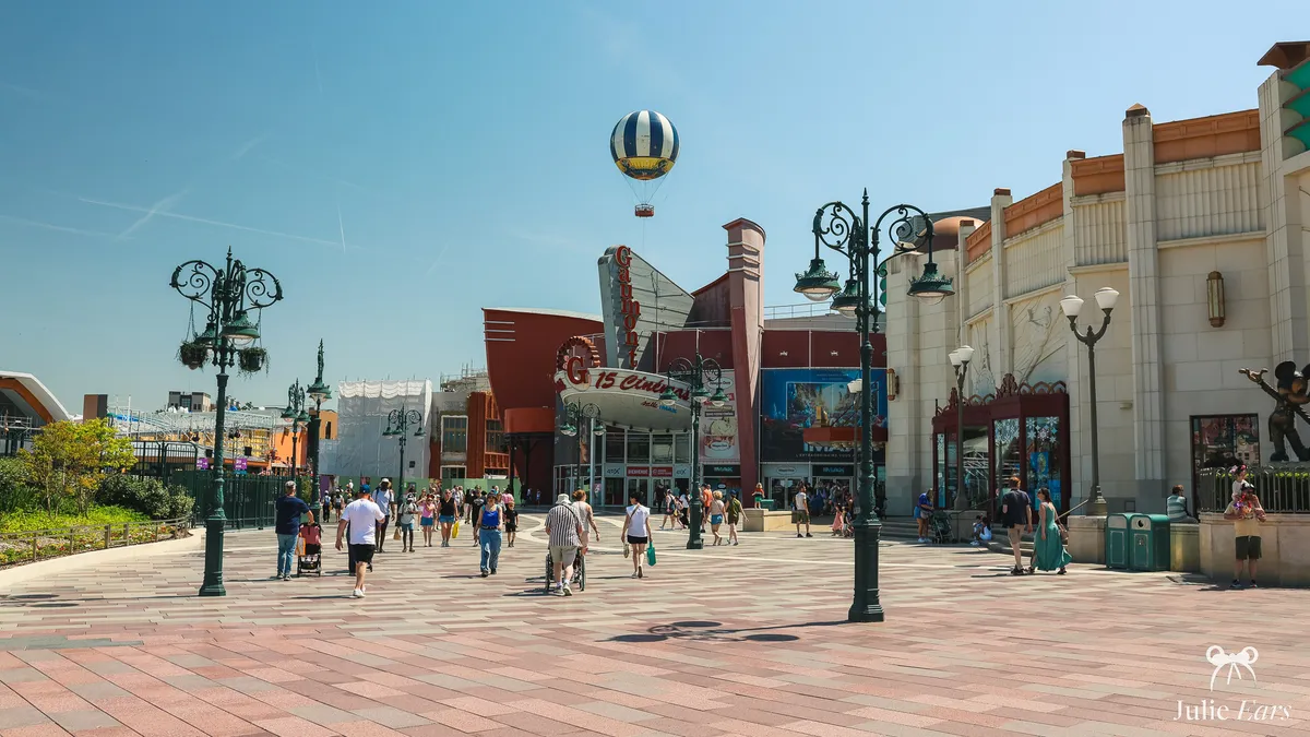 Gaumont cinema facade with its 15-screen sign at Disney Village in daylight, with street lamps and the striped tethered balloon in a blue sky