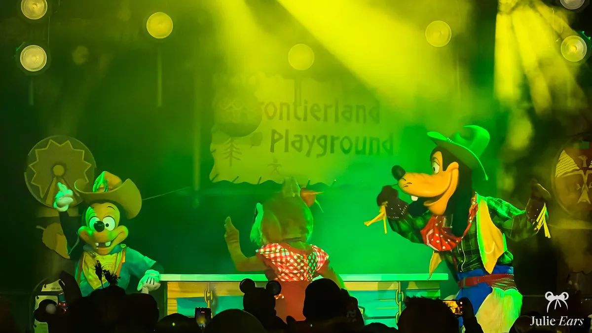 Goofy in a cowboy outfit with two other characters on the Frontierland Playground stage at Disneyland Paris, in smoke and green light