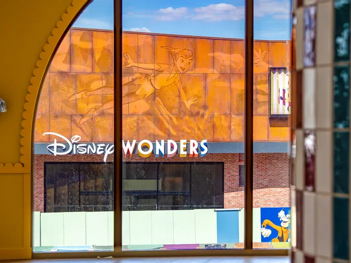 Disney Wonders shop at Disney Village seen through an arched window: copper Peter Pan panels, a multicoloured sign and a Goofy hoarding below