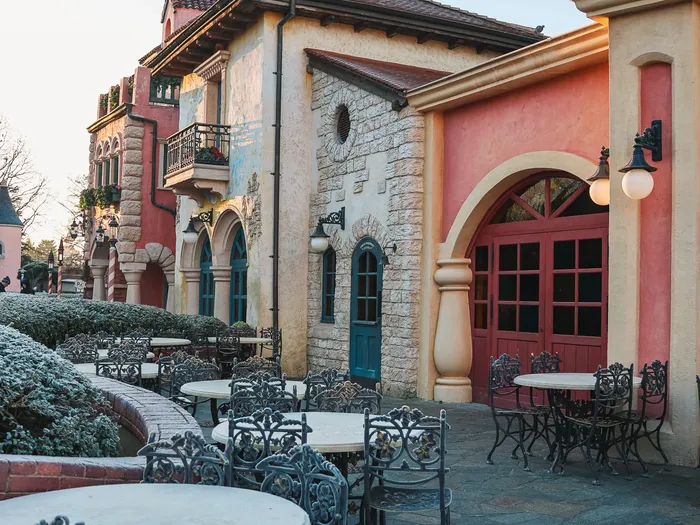Terrasse pavée aux tables en fer forgé de la Pizzeria Bella Notte, façade méditerranéenne au lever du jour à Fantasyland