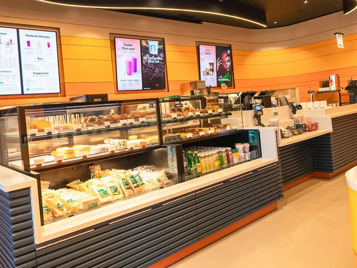 Starbucks counter at Disney Hotel Santa Fe, Disneyland Paris: display cases of sandwiches and pastries in front of an orange wall and menu boards
