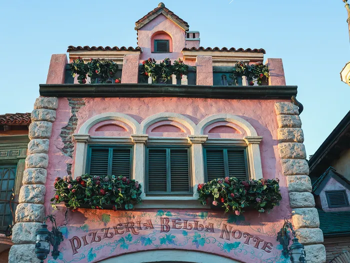 Façade rose à l’italienne de la Pizzeria Bella Notte, jardinières fleuries et enseigne peinte, à Fantasyland.