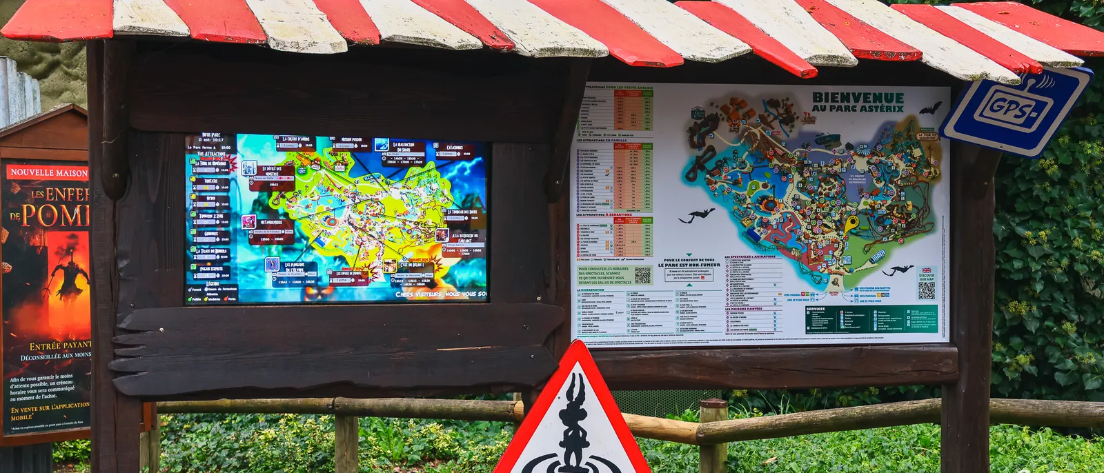 Panneau d'orientation en bois du Parc Astérix, toit rayé rouge et blanc, deux plans du parc affichés sous un repère GPS