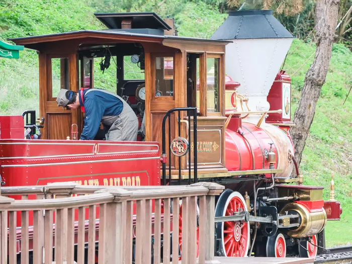 Locomotive à vapeur rouge du Disneyland Railroad en gare de Frontierland, un mécanicien penché sur la cabine.