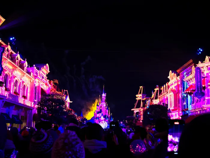 Projections roses et violettes sur les façades de Main Street vers le château pendant Disney Tales of Magic au Parc Disneyland.