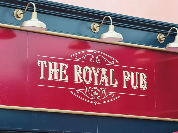 Enseigne rouge et dorée The Royal Pub éclairée par trois lampes, sur la façade du restaurant au Disney Village