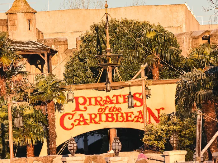 Banderole jaune Pirates of the Caribbean tendue au-dessus du pont de pierre, fort et palmiers dans la lumière dorée