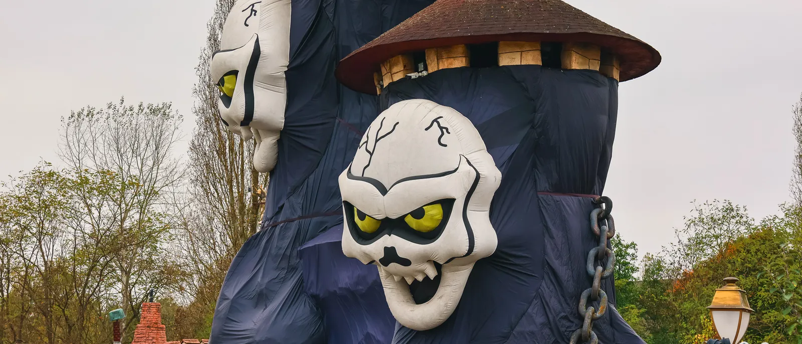 Décor d’Halloween géant, deux crânes blancs aux yeux jaunes émergeant d’une toile violette drapée sur une tour du parc
