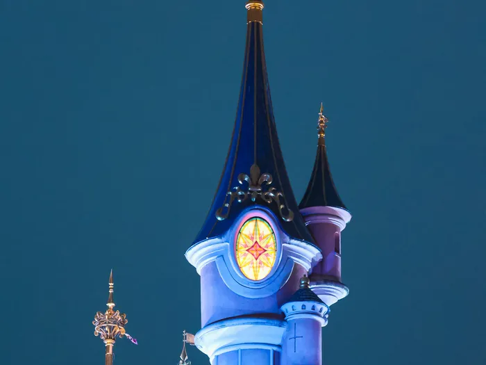 Flèches du Château de la Belle au Bois Dormant illuminées de bleu sous un ciel de nuit.