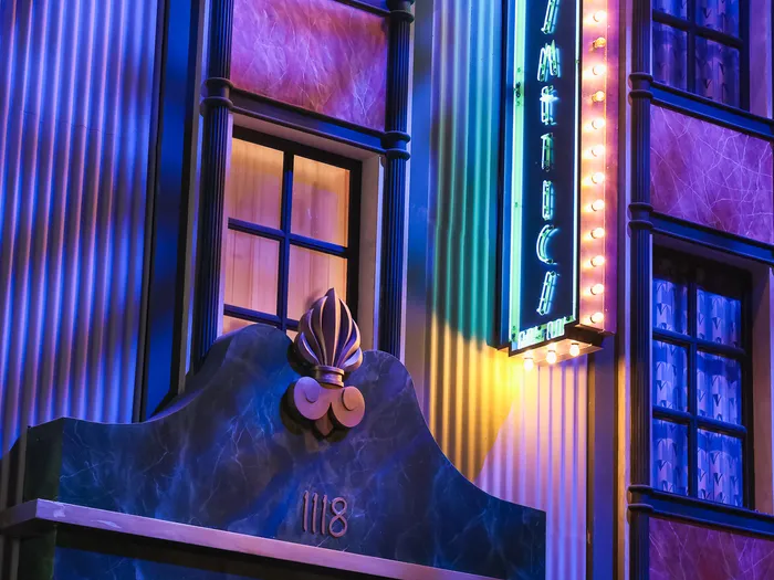 Art Deco frontage lit in blue and purple, with a round "Glamour Girl" sign, a vertical neon edged with bulbs and the number 1118, at Disneyland Paris.