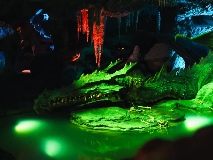 Dragon endormi au bord d’un bassin vert dans la grotte sombre de La Tanière du Dragon, sous les stalactites.