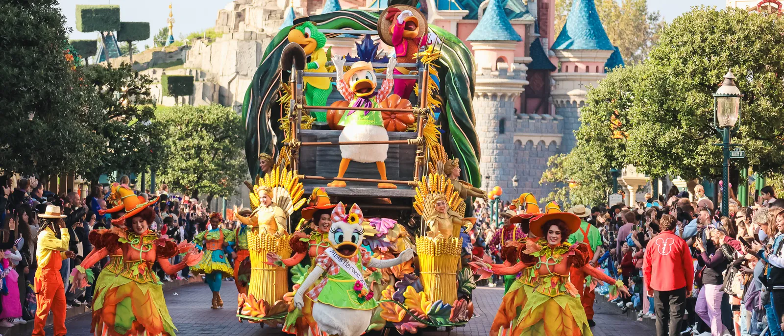 Daisy et Donald mènent une parade d’Halloween de jour avec des danseurs en costumes d’automne, château derrière.