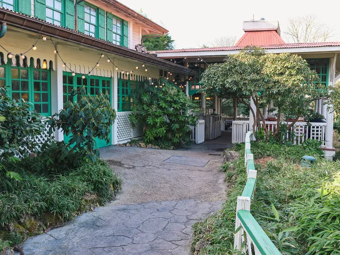 Façade aux volets verts et guirlandes lumineuses du Colonel Hathi’s, allée bordée de plantes à Adventureland.