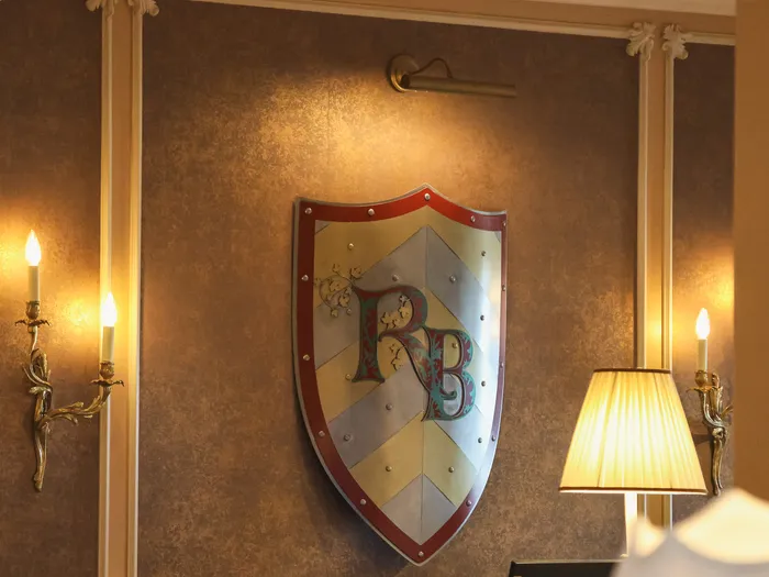 Écusson peint aux initiales RB accroché au mur du Royal Banquet au Disneyland Hotel, entre deux appliques à bougies
