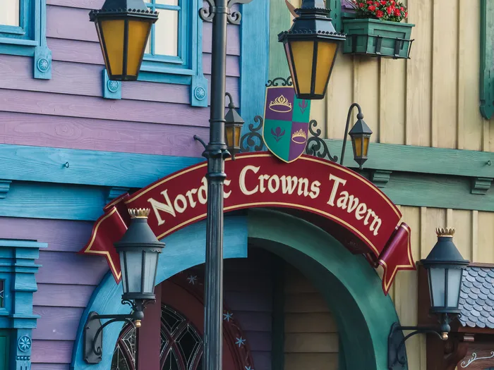 Enseigne blasonnée de la Nordic Crowns Tavern devant les maisons nordiques colorées de World of Frozen