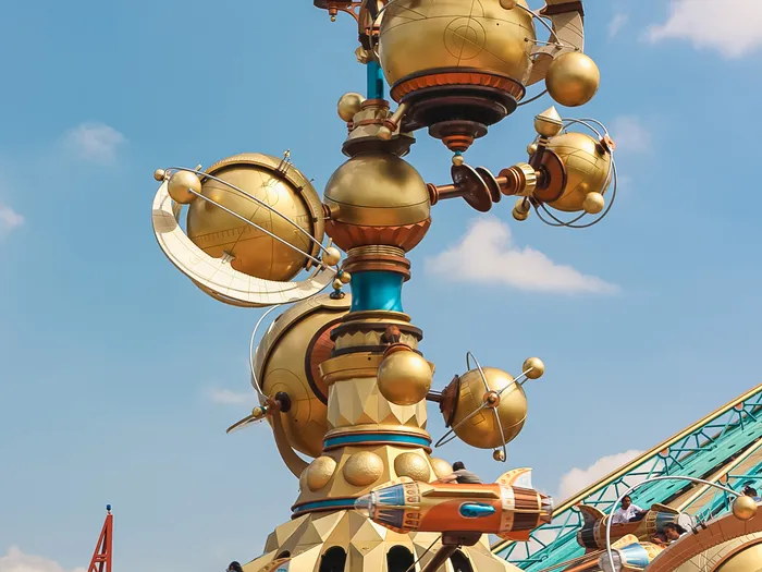 Mât central doré d’Orbitron avec ses planètes et anneaux, entouré de nacelles fusées en pleine rotation à Discoveryland.
