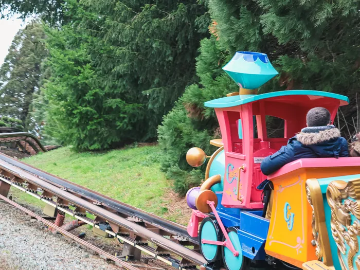 Le petit train du cirque Casey Jr. avec ses passagers sur les rails bordés de sapins à Fantasyland
