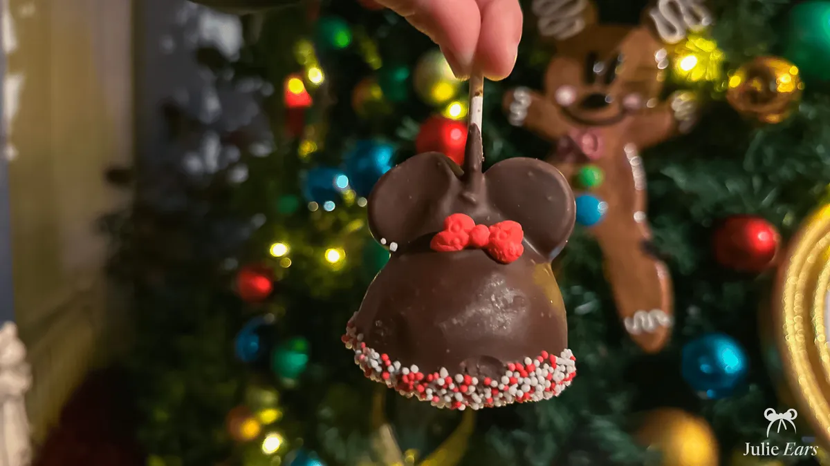 Cake pop en forme de Minnie enrobée de chocolat et de vermicelles de fête, devant un sapin de Noël à Disneyland Paris