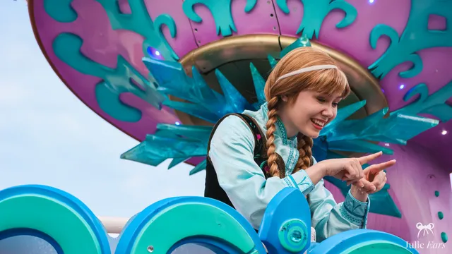 Anna, tresses rousses et tenue turquoise, sourit sur le char de la parade La Reine des Neiges à Disneyland Paris.