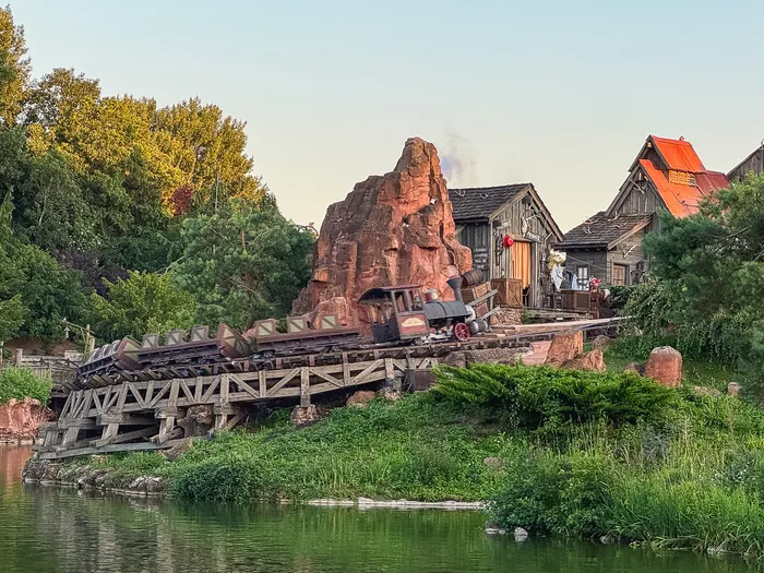 Train à vapeur de Big Thunder Mountain franchissant un pont en bois au-dessus du lac, montagne rouge en fond